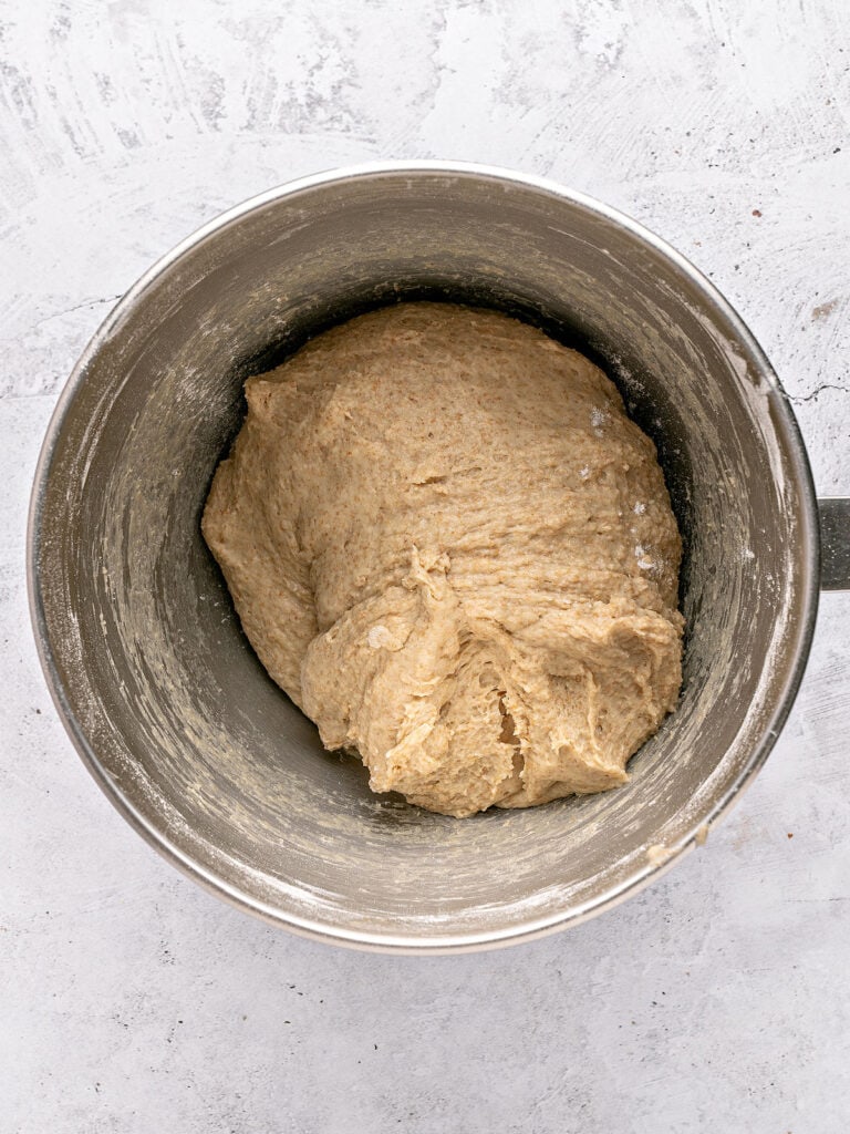 Stand mixer bowl with whole wheat bread dough. Light gray surface.