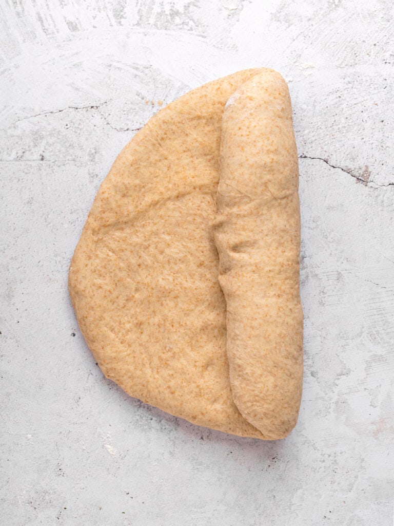 Half rolled whole wheat bread dough on a light gray surface.