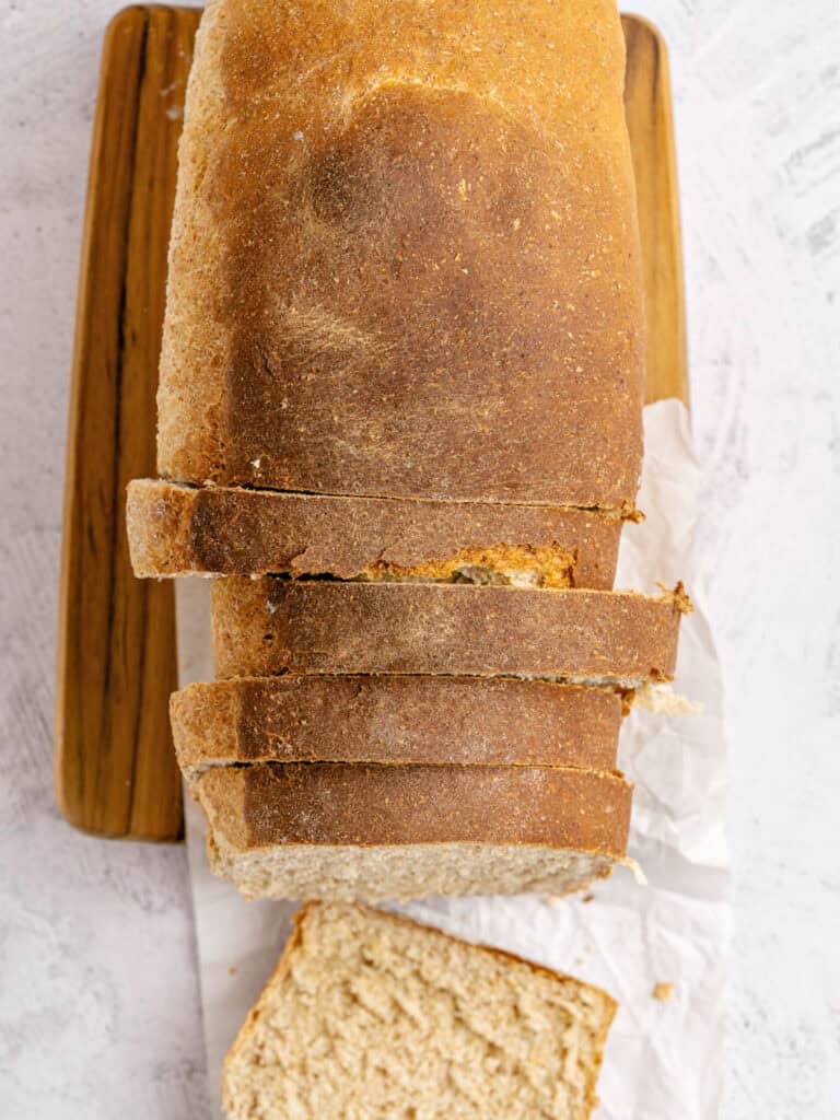 Top view of sliced loaf of whole wheat bread on a wooden board.
