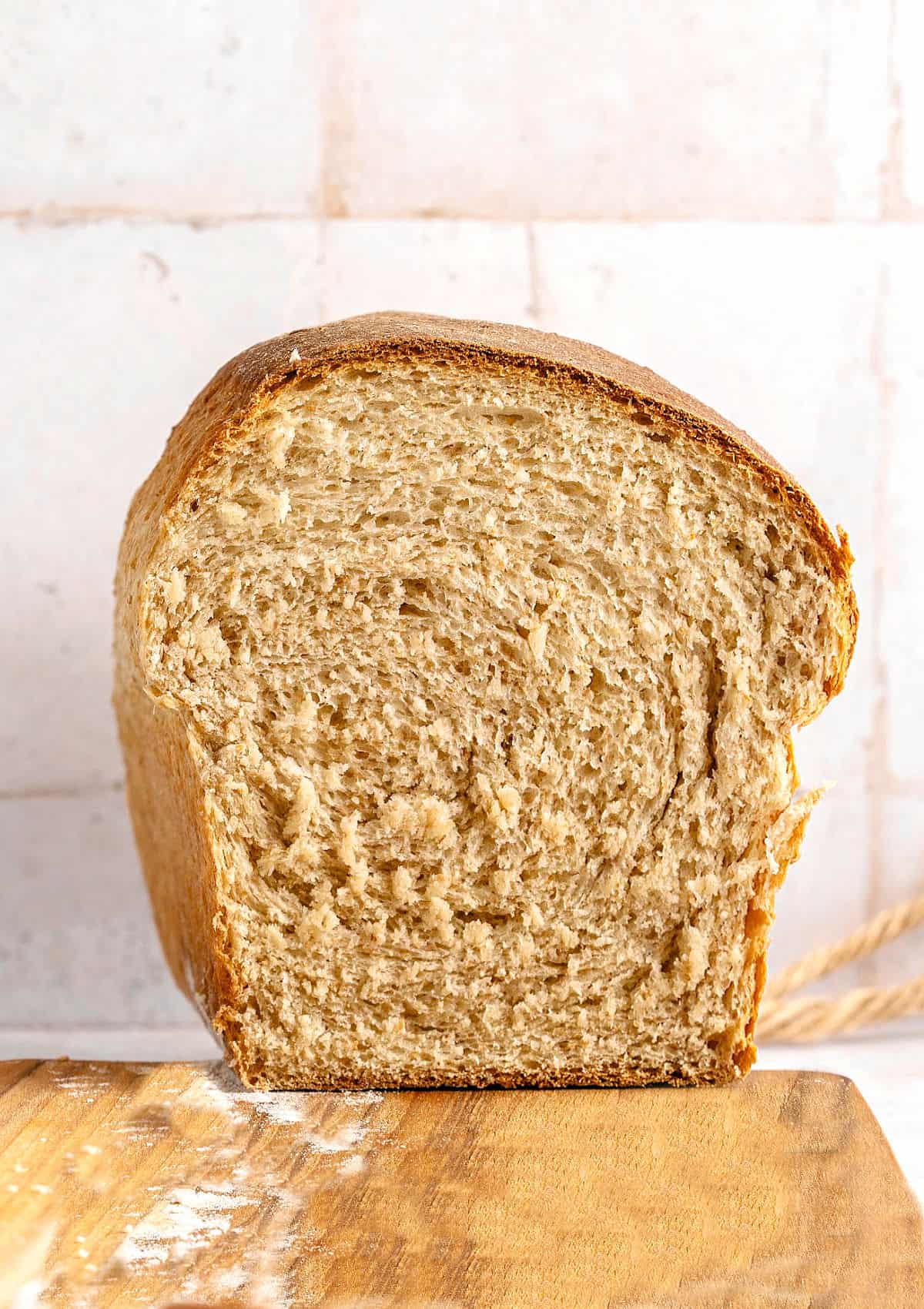 Front view of halved whole wheat loaf on a wooden board. Tile background.