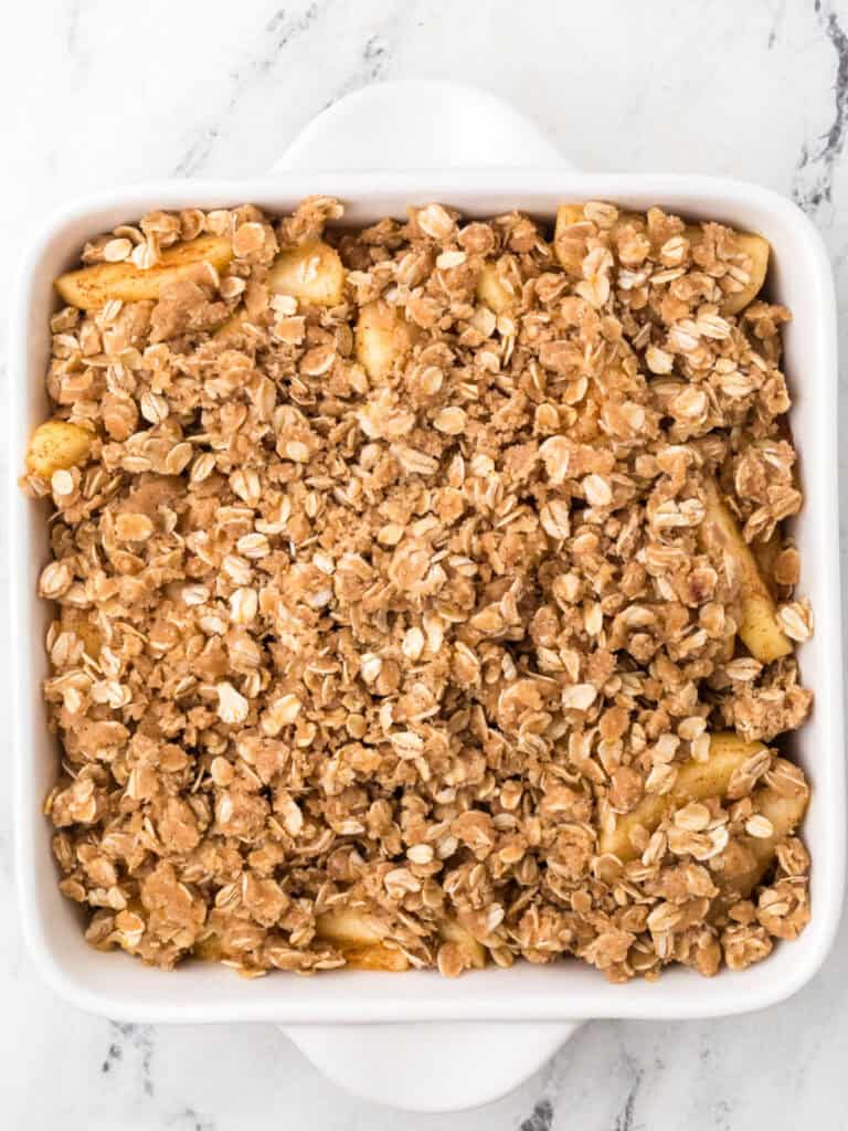 Old-fashioned apple crisp in a white dish before baking.