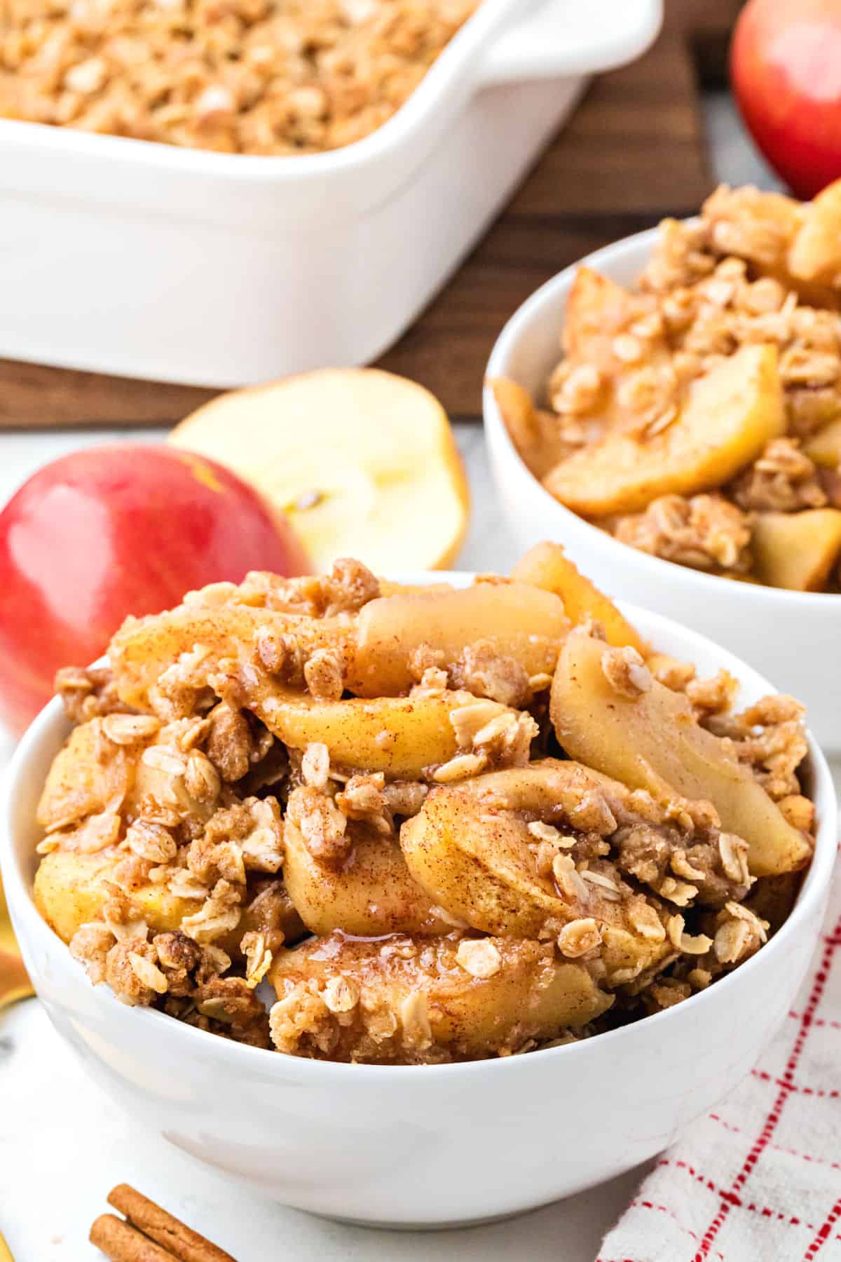 Apple crisp with oats in white bowls. Halved red apples.