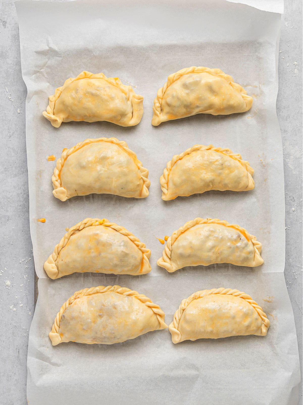 Egg-washed empanadas on parchment paper before baking.