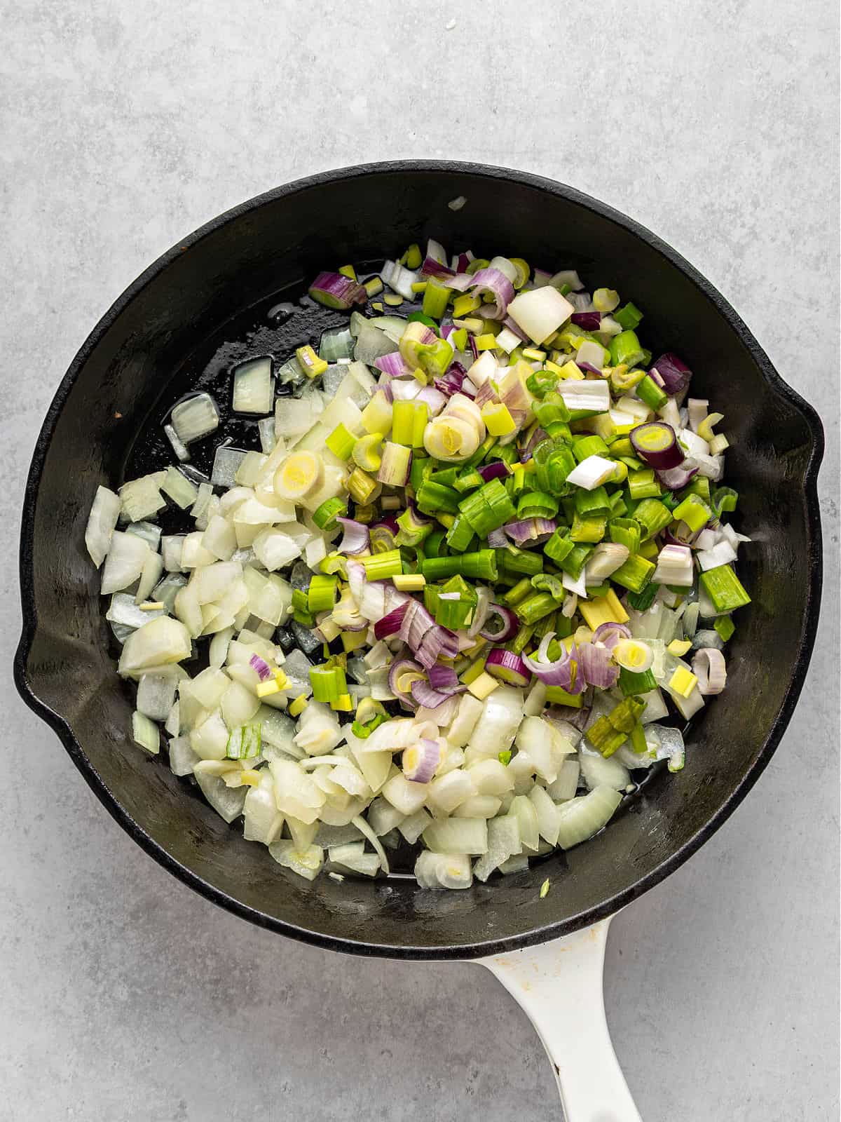 Black skillet with three types of onion. Light gray background.