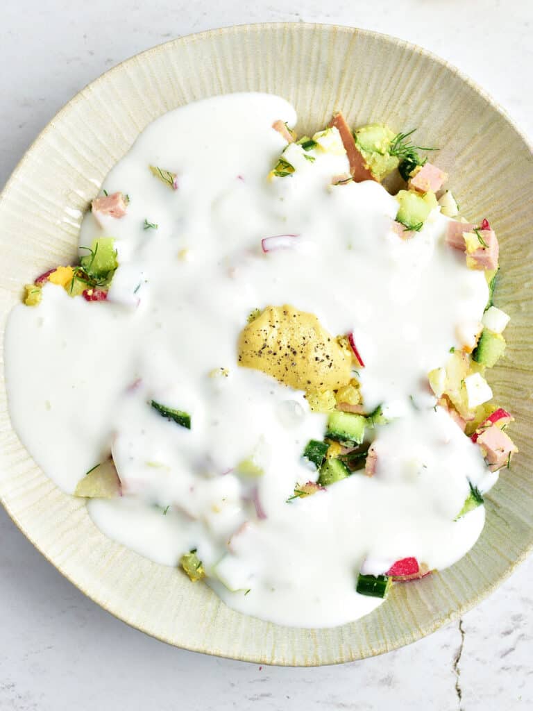 Yogurt topped vegetables in a cream-colored bowl.