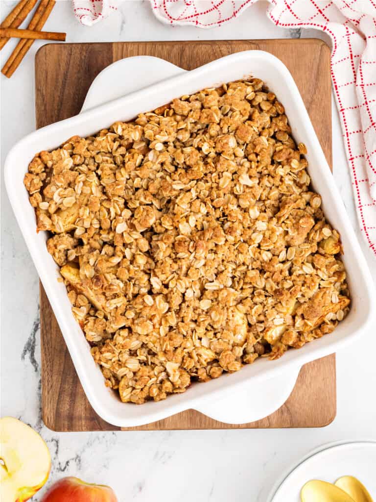 Square white ceramic dish with apple oat crisp. Wooden board, white background.