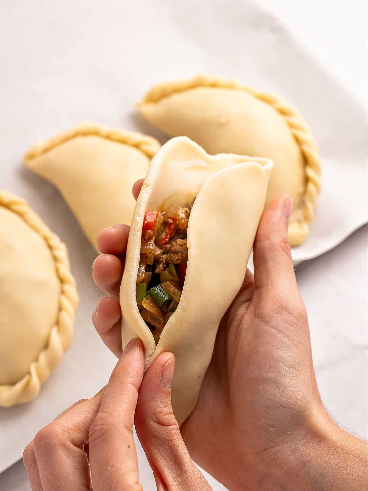 Closing an empanada dough in half with meat filling.