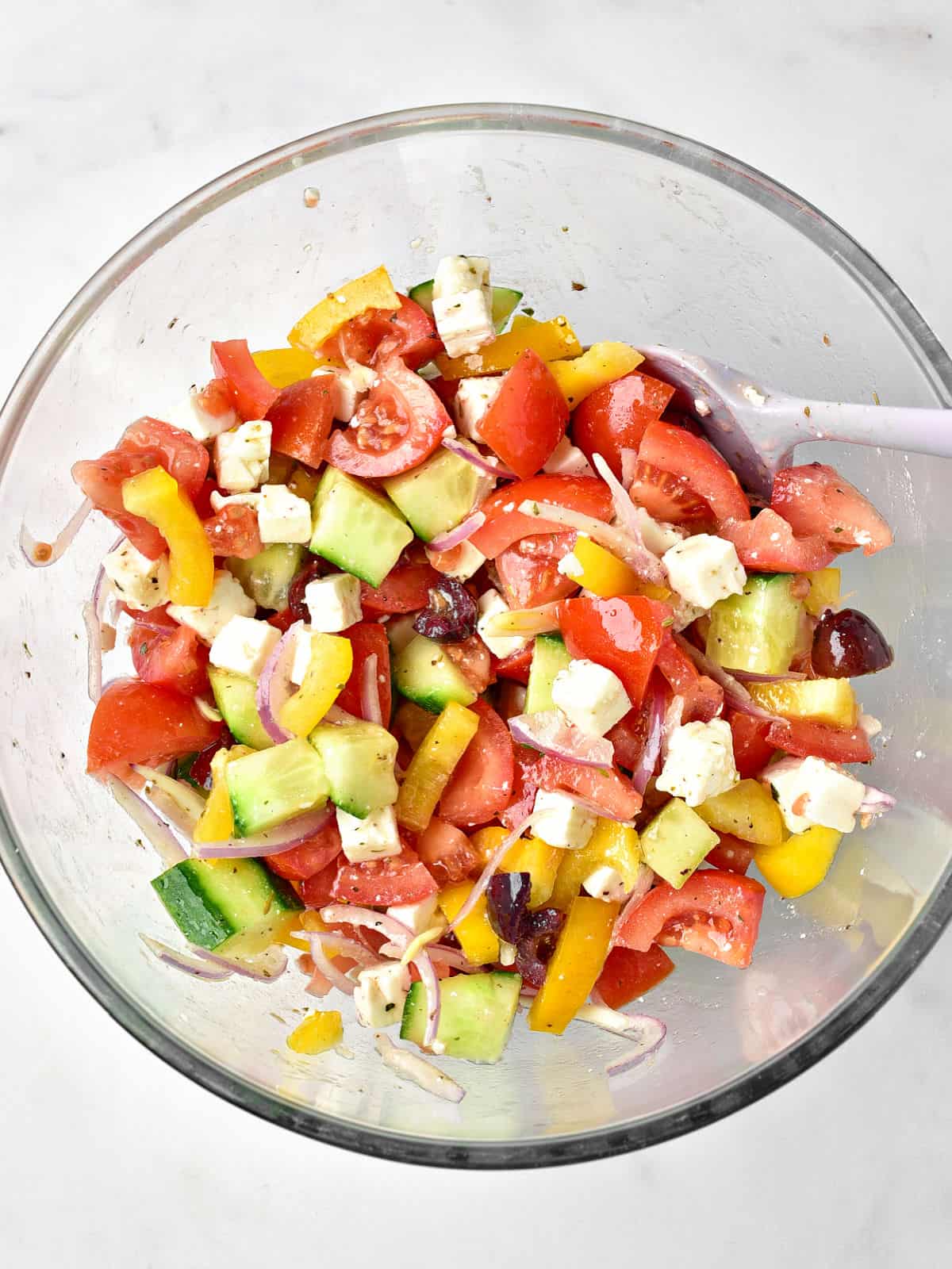 Tossed Greek salad in a glass bowl. White background.
