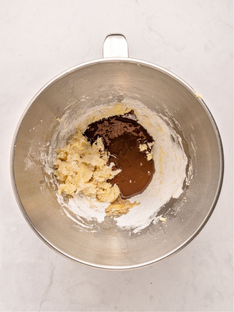 Butter, powdered sugar and melted chocolate in a metal mixing bowl. White background.