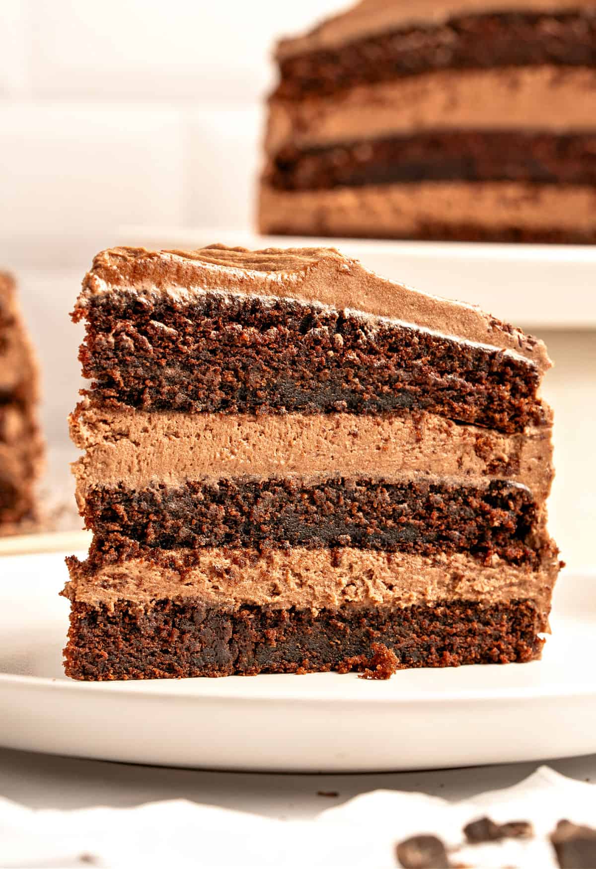 Slice of triple layer chocolate cake with old fashioned frosting. White plate.