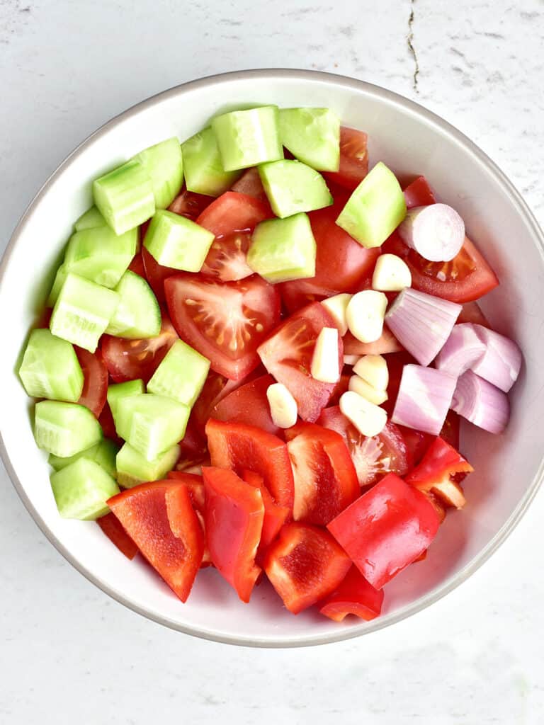 White bowl with chopped cucumber, red onion, red peppers, tomatoes.