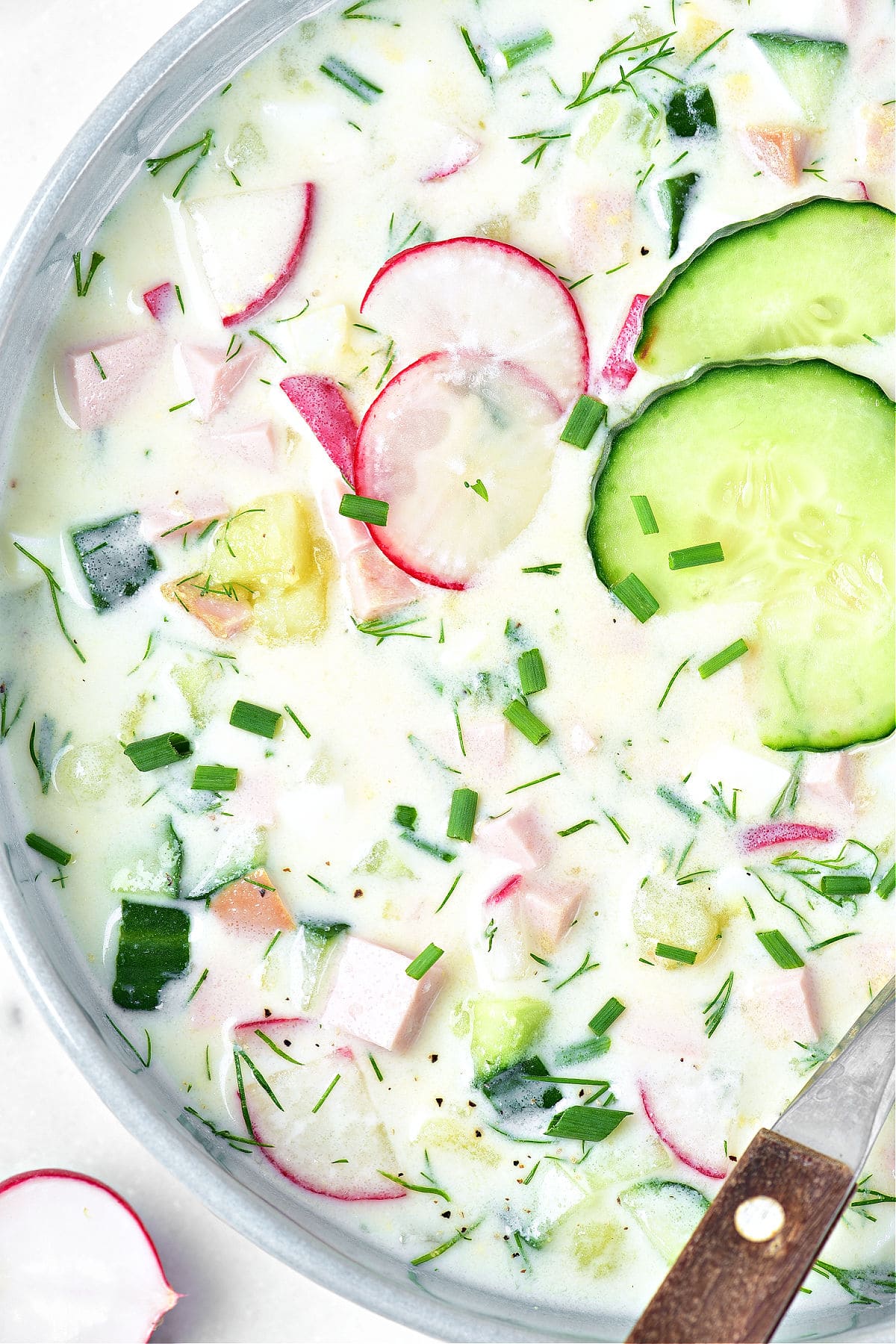 Close up gray bowl with Russian soup featuring kefir, cucumbers, herbs and radishes.