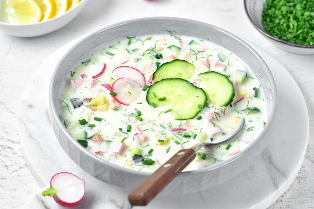 White marble with gray bowl of cucumber, yogurt, radish, dill and ham soup.