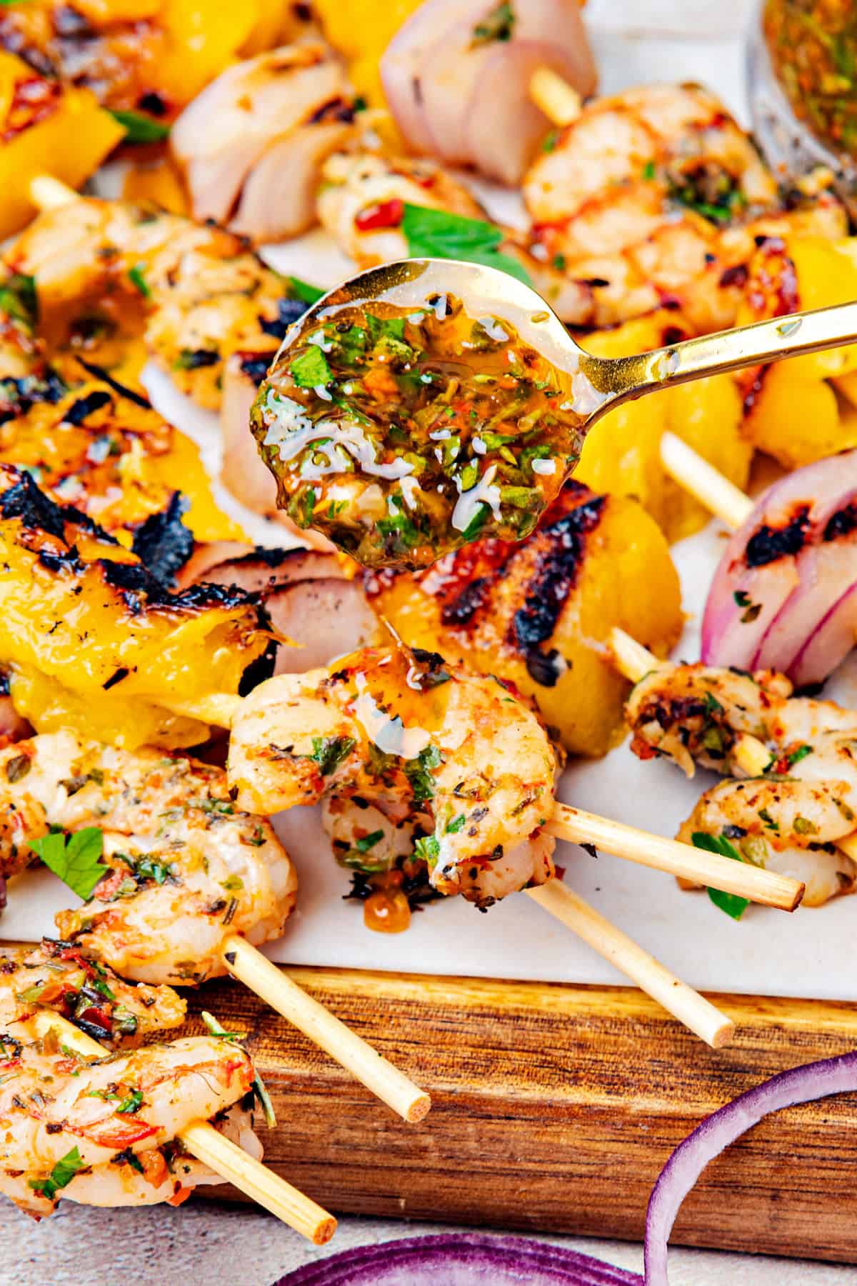 Spooning chimichurri on shrimp onion mango skewers.