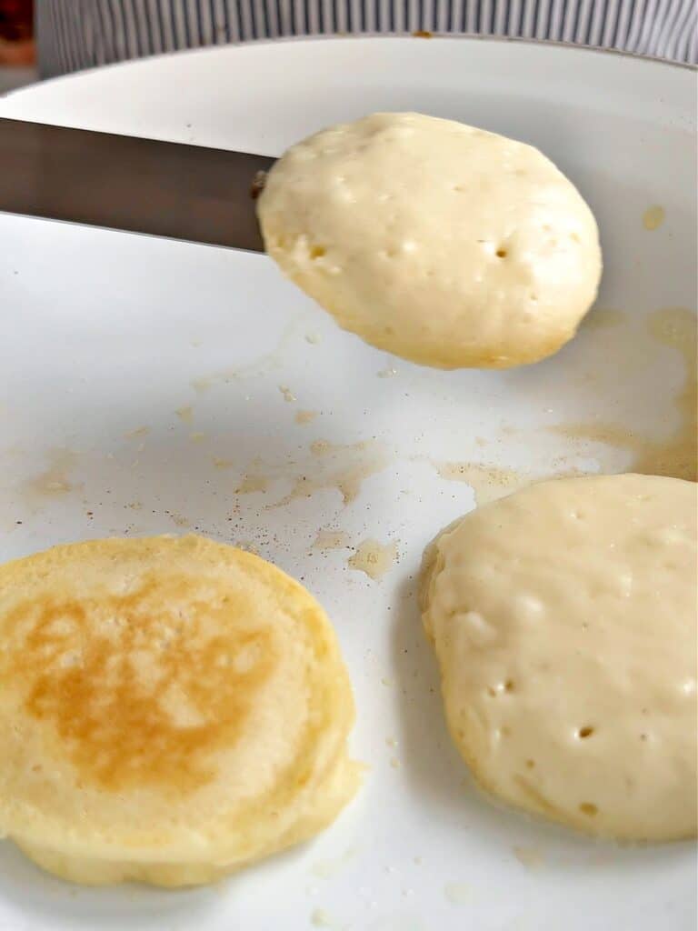 Lifting mini pancake with spatula. White skillet, more pancakes.