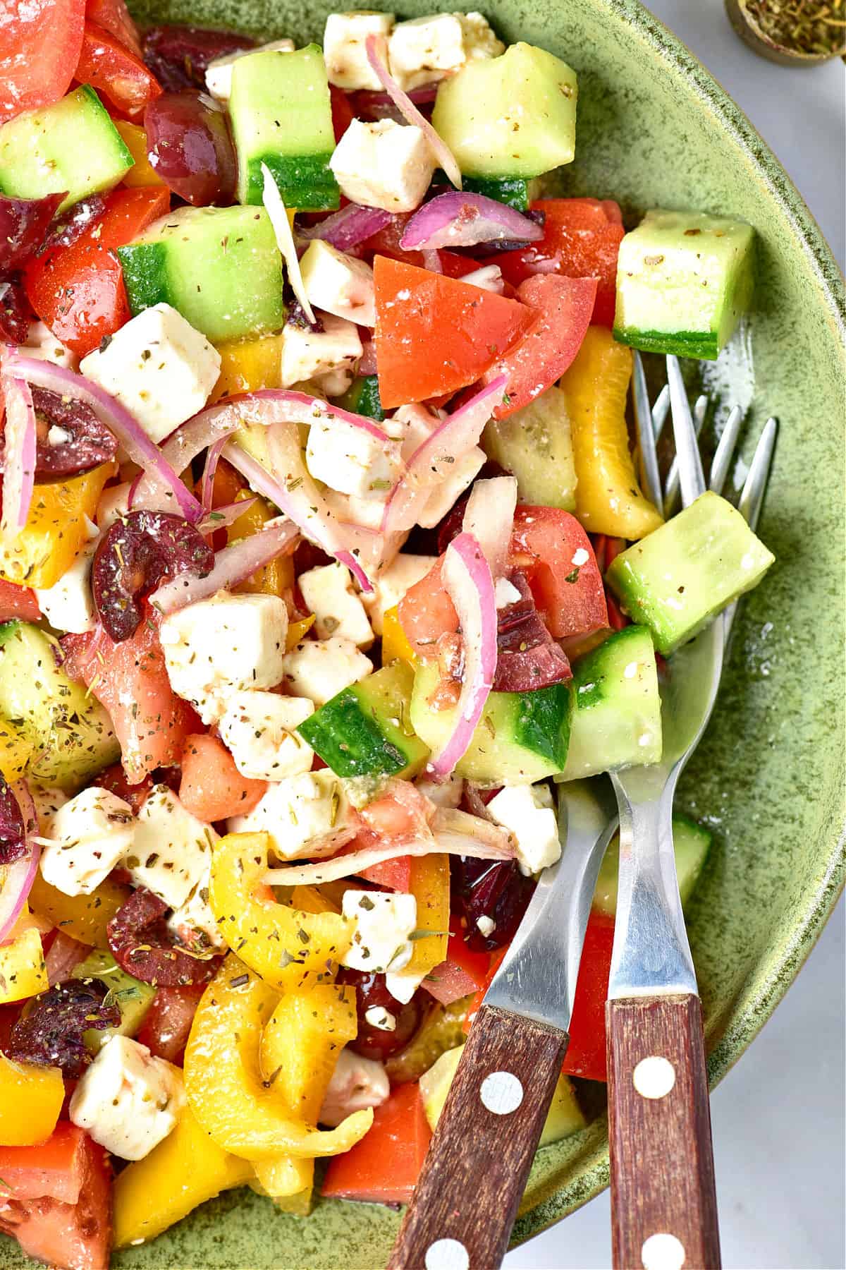 Close up of Greek salad on a green plate. Silver wood utensils.