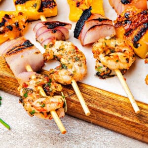 Close up grilled chimichurri shrimp skewers on a wooden board.