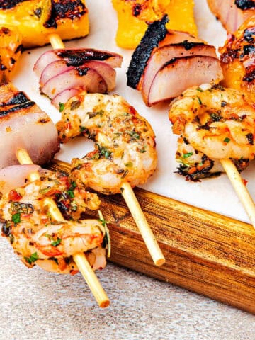 Close up grilled chimichurri shrimp skewers on a wooden board.