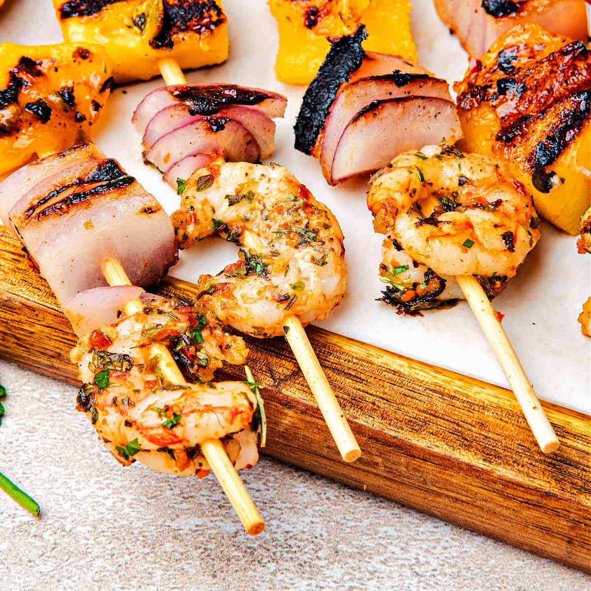 Close up grilled chimichurri shrimp skewers on a wooden board.