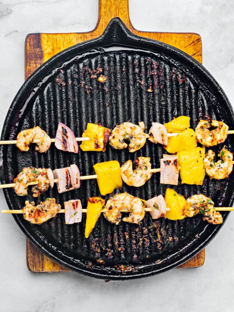 Black grill skillet with shrimp skewers on a wooden board.