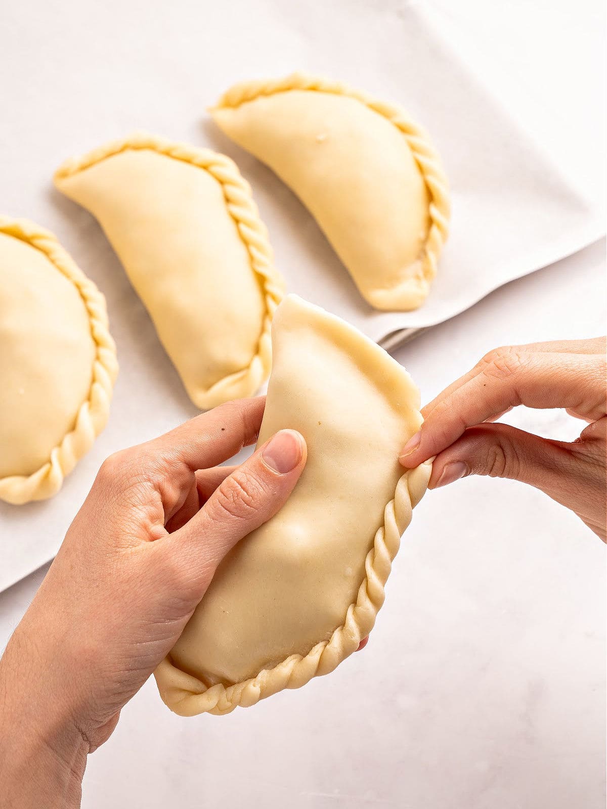 Crimping beef empanadas on a white surface.