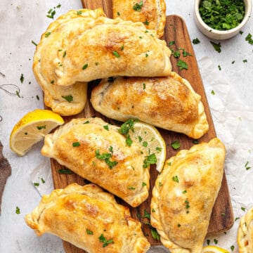 Several beef empanadas on a wooden board. White background. Sprinkled chopped parsley.