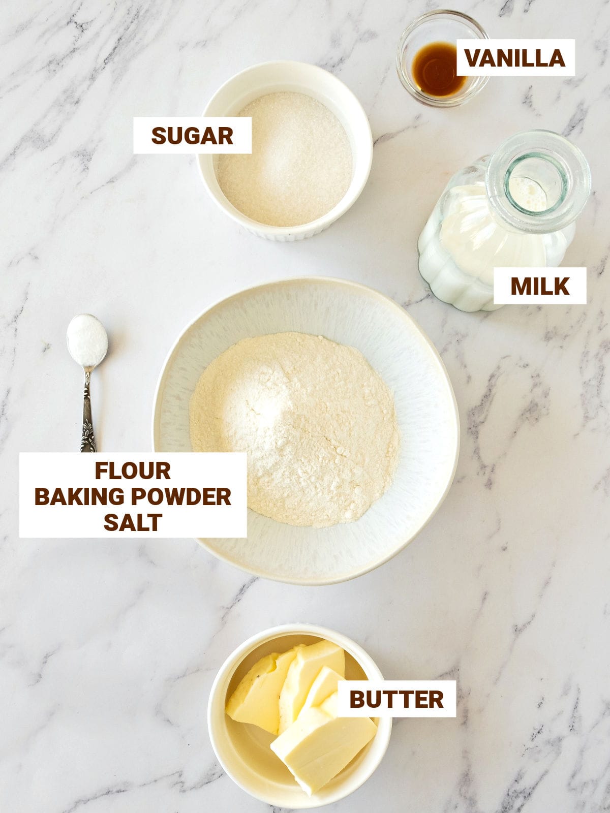 White marble surface with ingredients for pancakes in white bowls.
