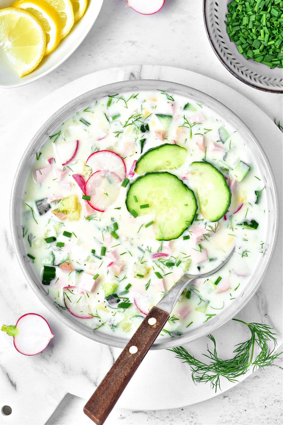 Light gray shallow plate with cold cucumber yogurt soup with dill and radishes. White background.