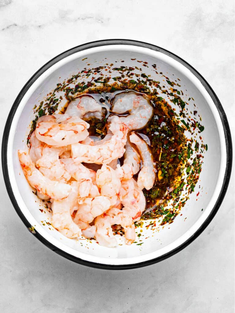 Enameled white bowl with raw shrimp and chimichurri.