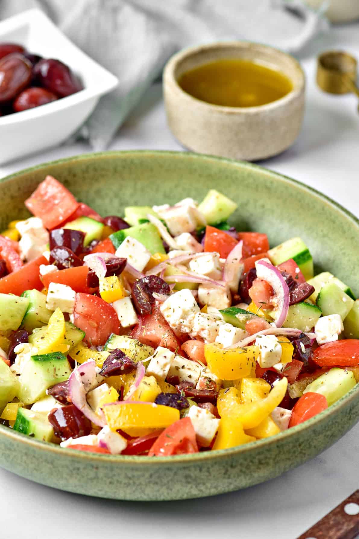 Serving of Greek salad on a green plate. Bowl with olives and dressing.