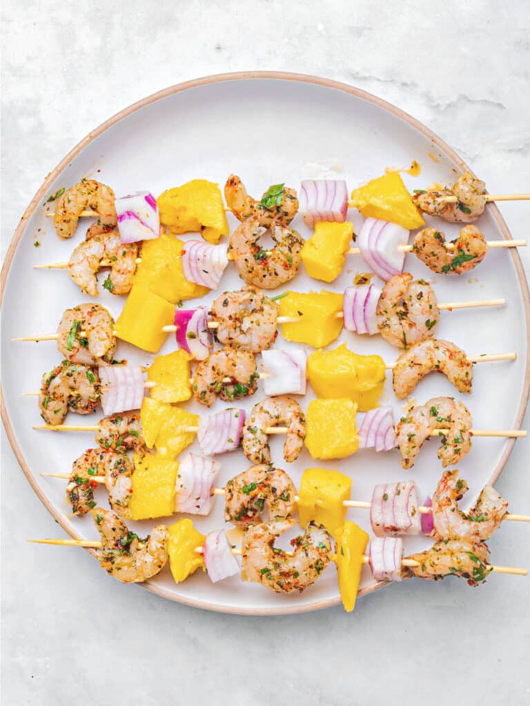 White plate with uncooked mango shrimp skewers.
