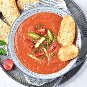 Metal tray with gray bowl of gazpacho and bread slices.