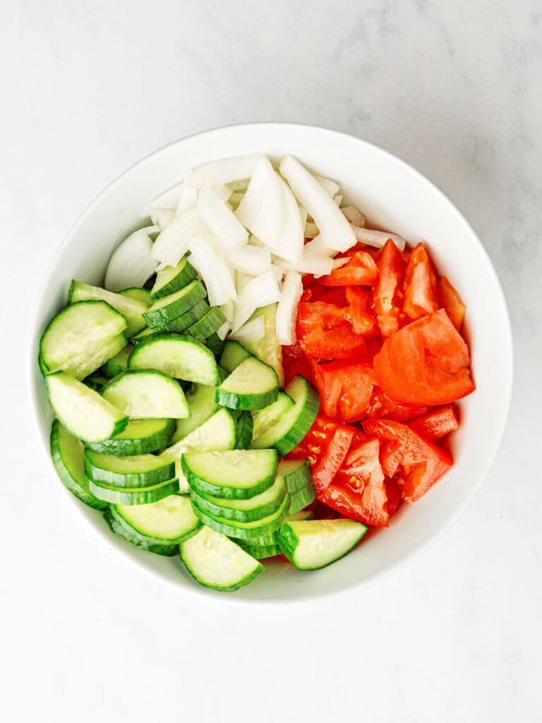 Chopped cucumber, tomato and onion in a white bowl.