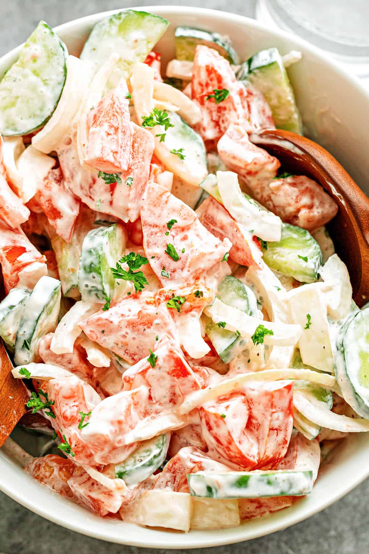 Tomato cucumber salad with creamy dressing in white bowl. 