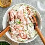 White bowl of creamy cucumber tomato salad. Wooden utensils. Gray background.