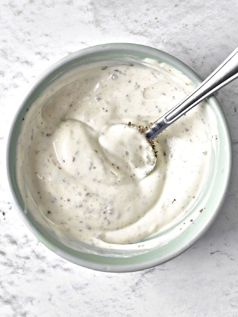 Gray bowl with creamy salad dressing. Silver spoon inside.