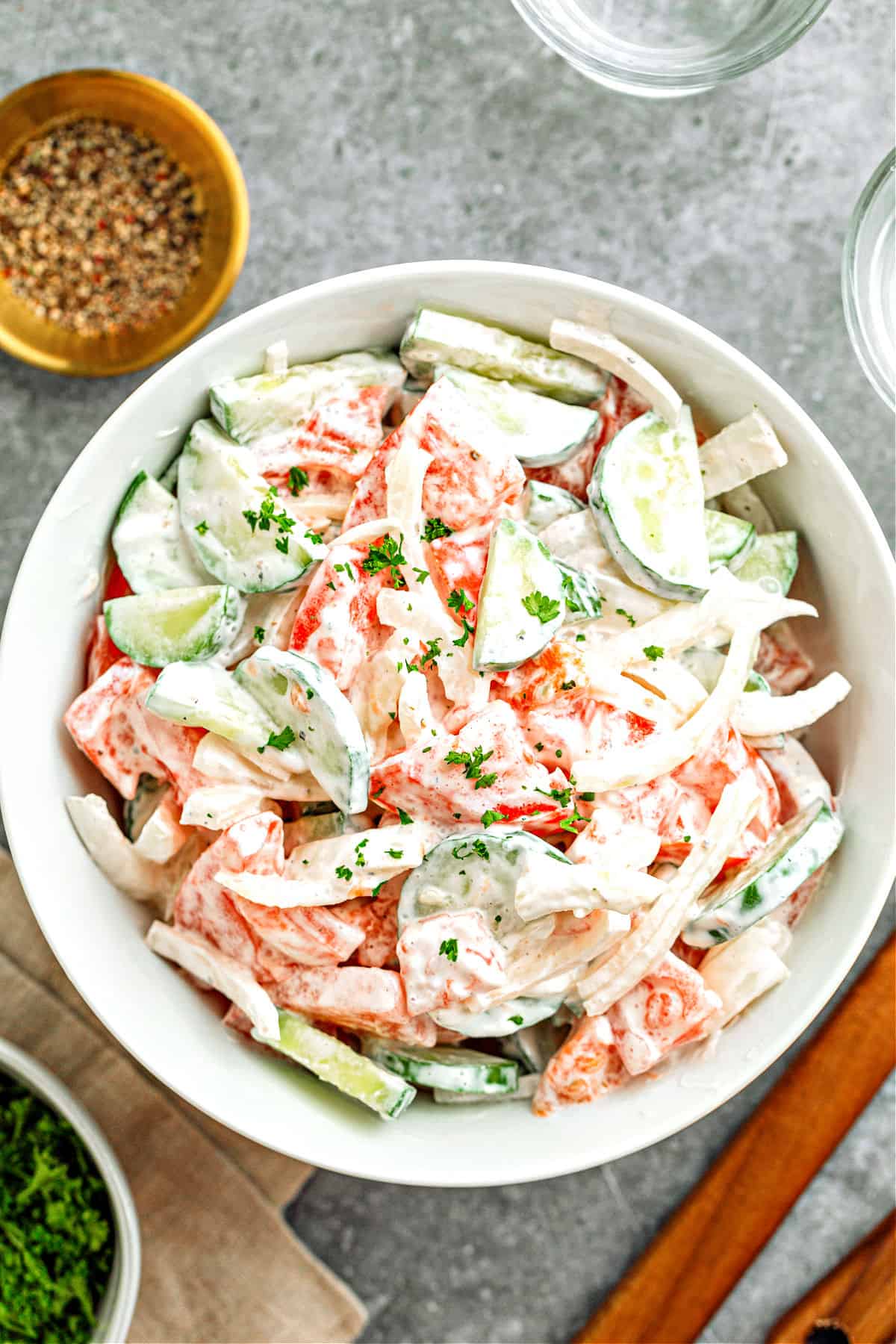 Gray background with white bowl of creamy tomato cucumber onion salad.