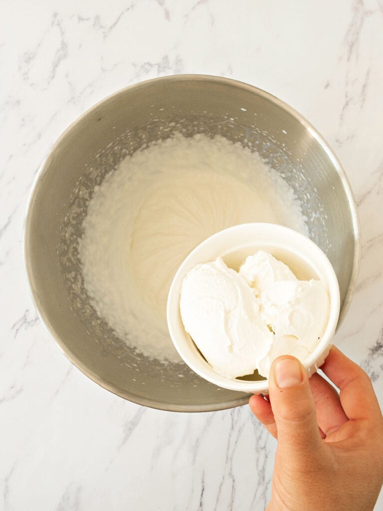 Adding sour cream to a metal bowl with whipped cream.