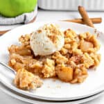 Old fashioned apple crumble served on a white plate with scoop of ice cream.