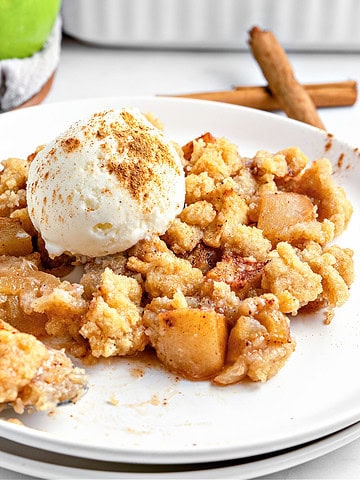 Old fashioned apple crumble served on a white plate with scoop of ice cream.