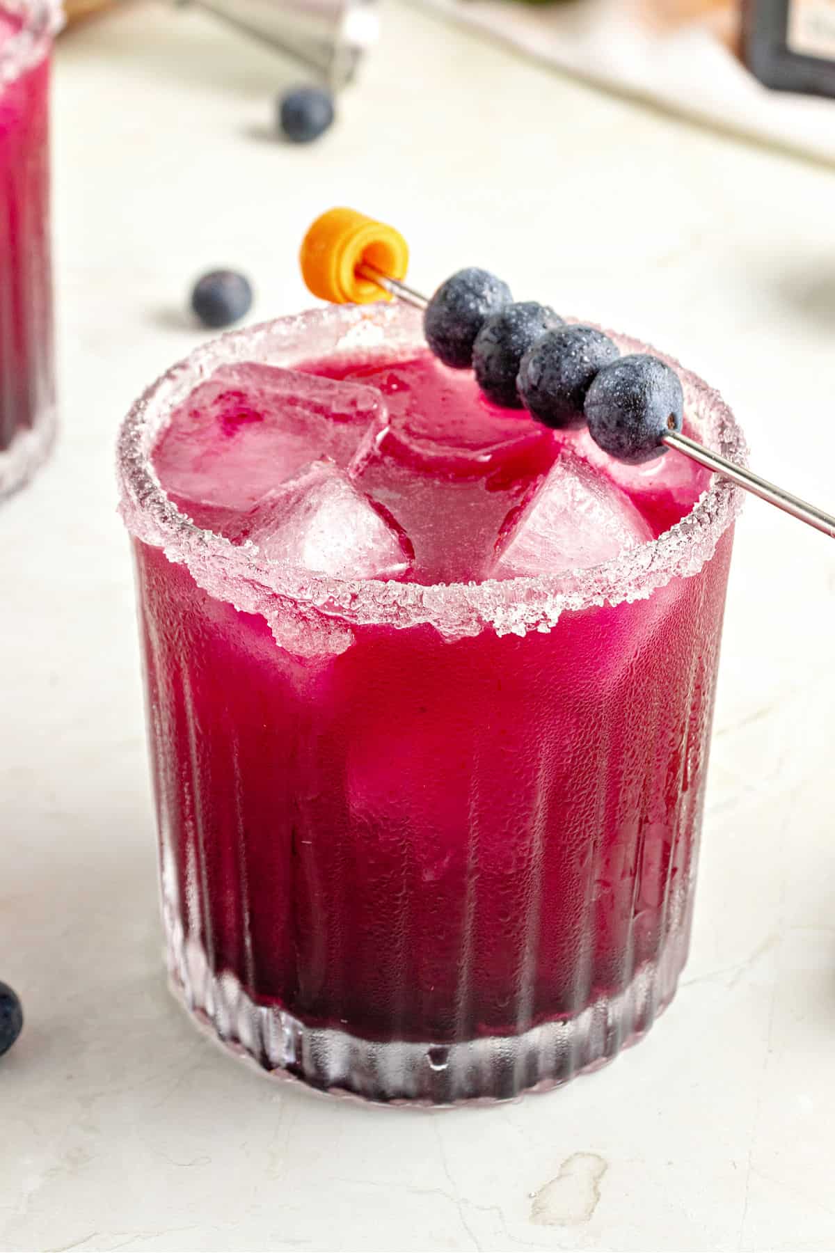 Close up glass of blueberry margarita. White marble background.