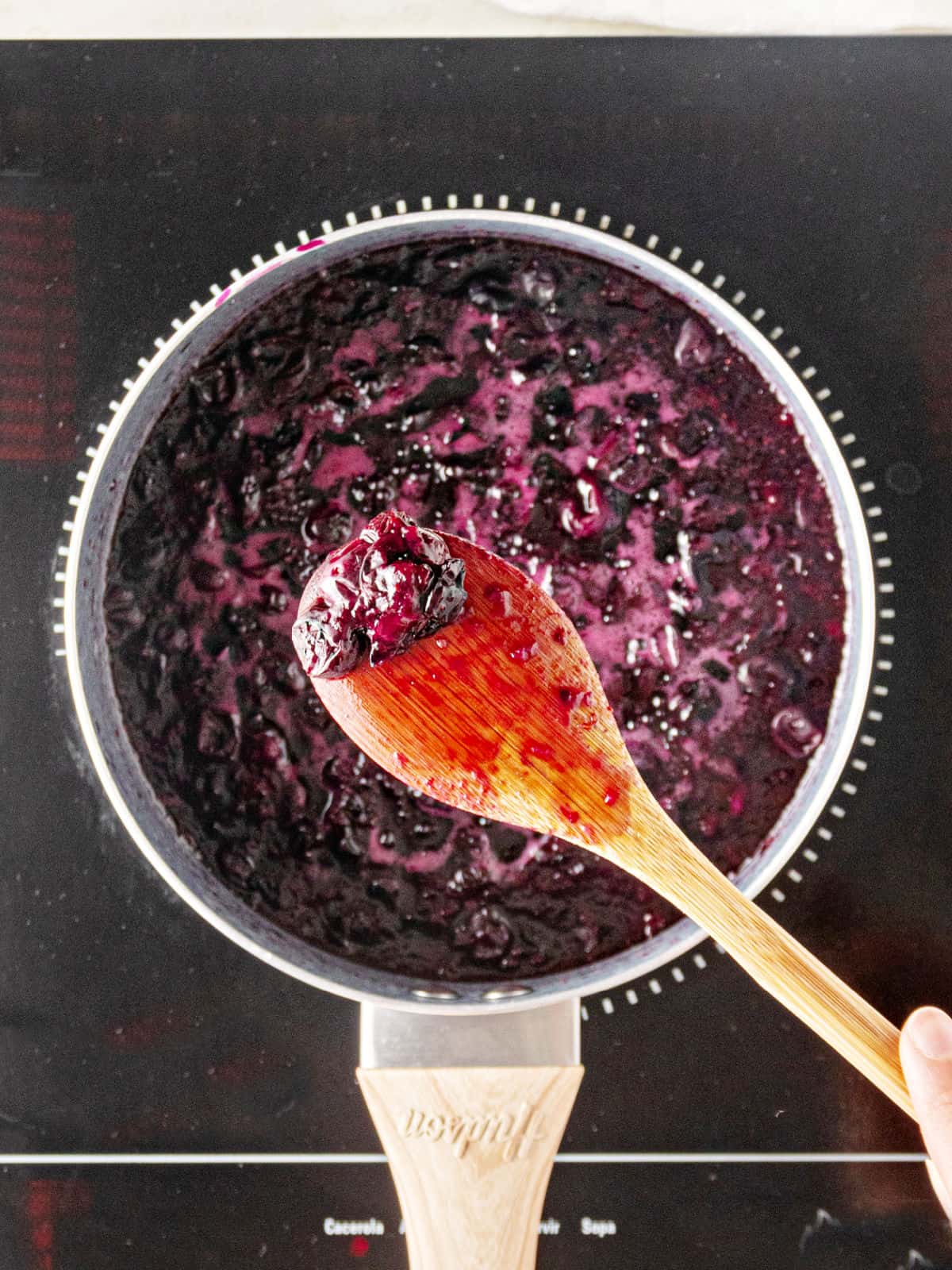Black portable burner with saucepan of blueberry sauce. Wooden spoon. 