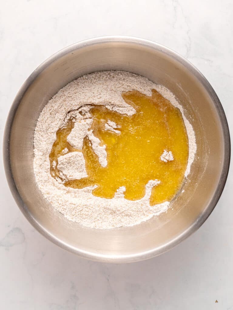 Melted butter and dry ingredients in a metal bowl. Top view. White background.