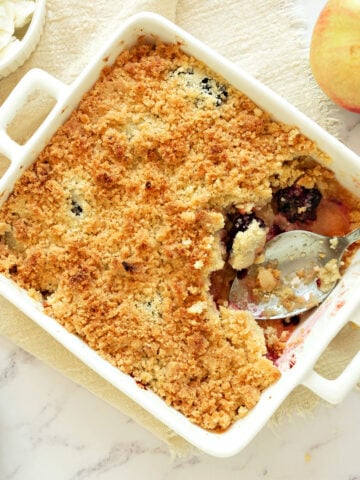 Square white dish with baked apple blackberry crumble. White background.