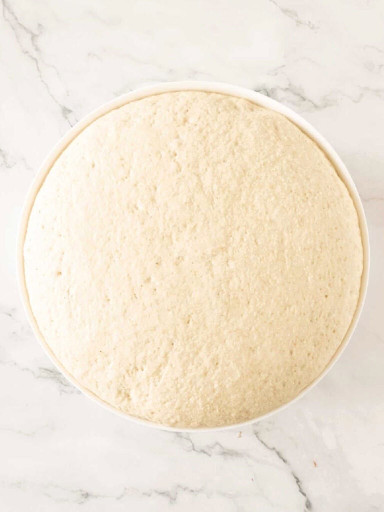White background with risen bread dough in a glass bowl.