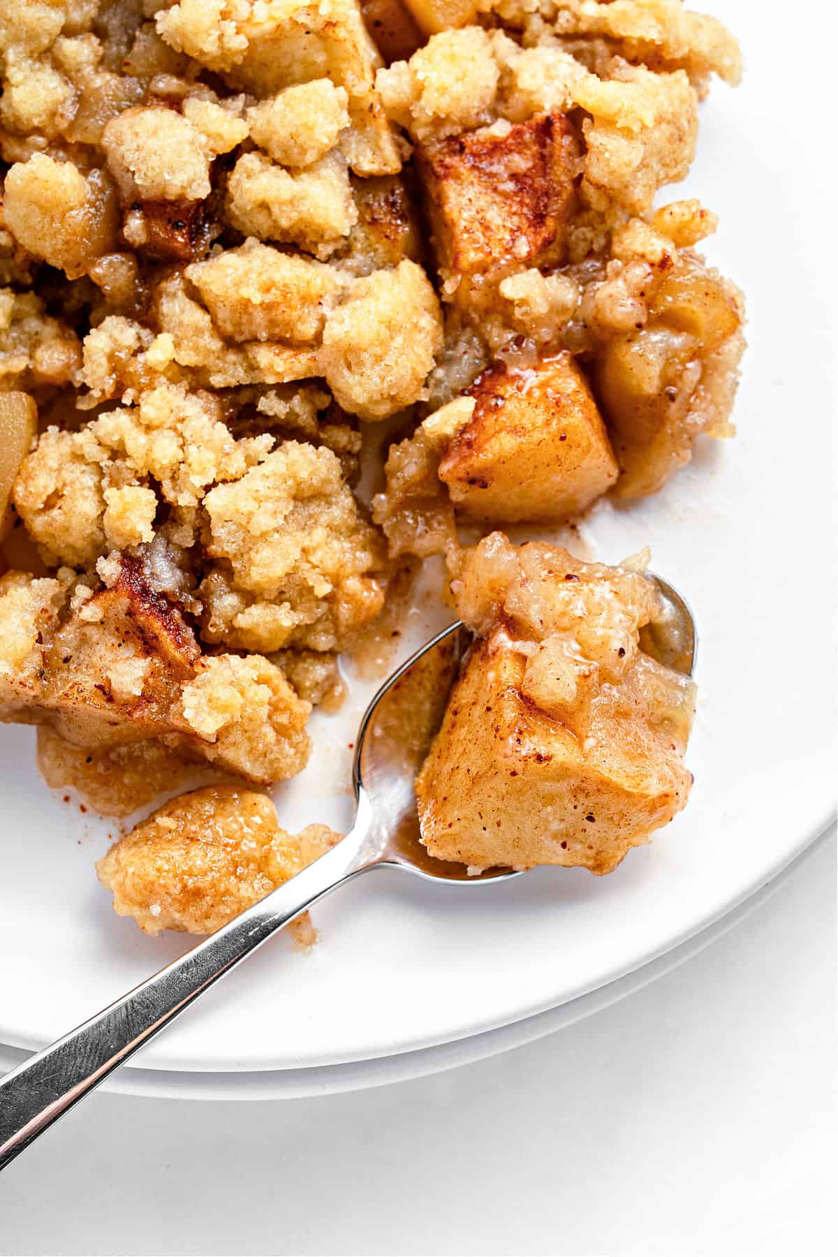 Close up serving of apple crumble on a white plate with a spoon.
