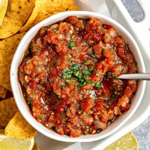 Close up white bowl with charred tomato salsa and corn chips.