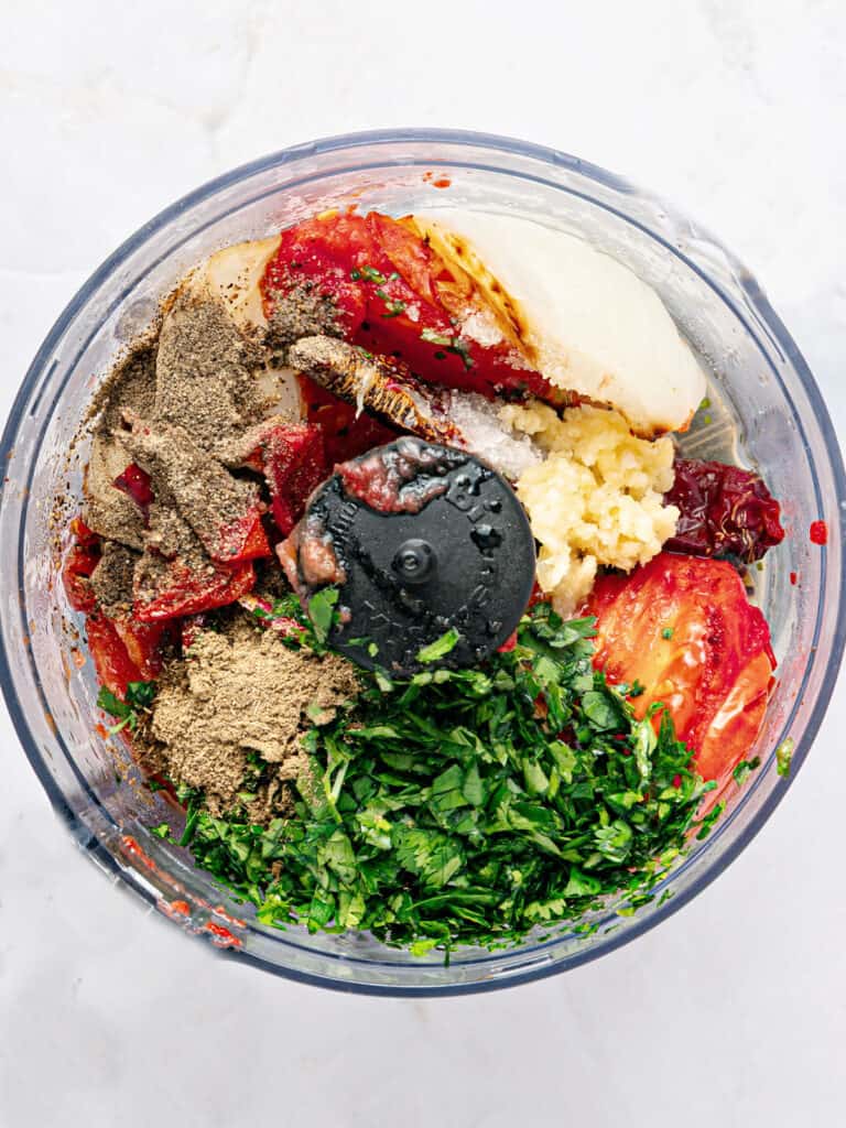 Food processor bowl with ingredients for roasted tomato, onion, cilantro salsa.