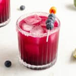 Glass of blueberry margarita on a white marbled surface.