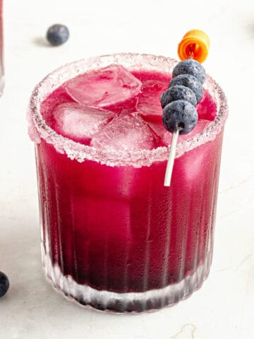Glass of blueberry margarita on a white marbled surface.
